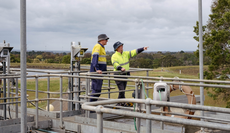 Two people in high vis on top of a walkway at the Hamilton Water Treatment Plant. One is pointing at something in the distance.